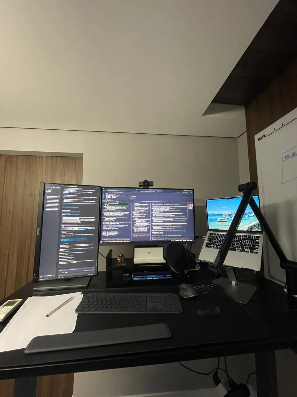 Office desk with two monitors full of code, a laptop and a microphone