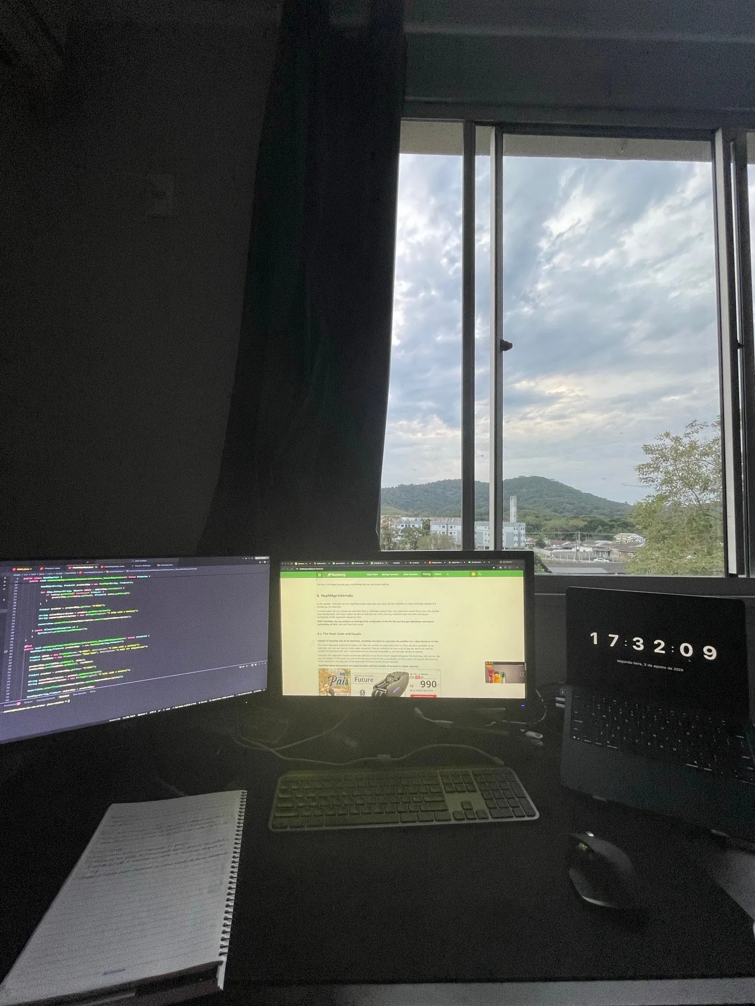Home desk: monitor with code, laptop and a window overlooking the hills of Florianópolis