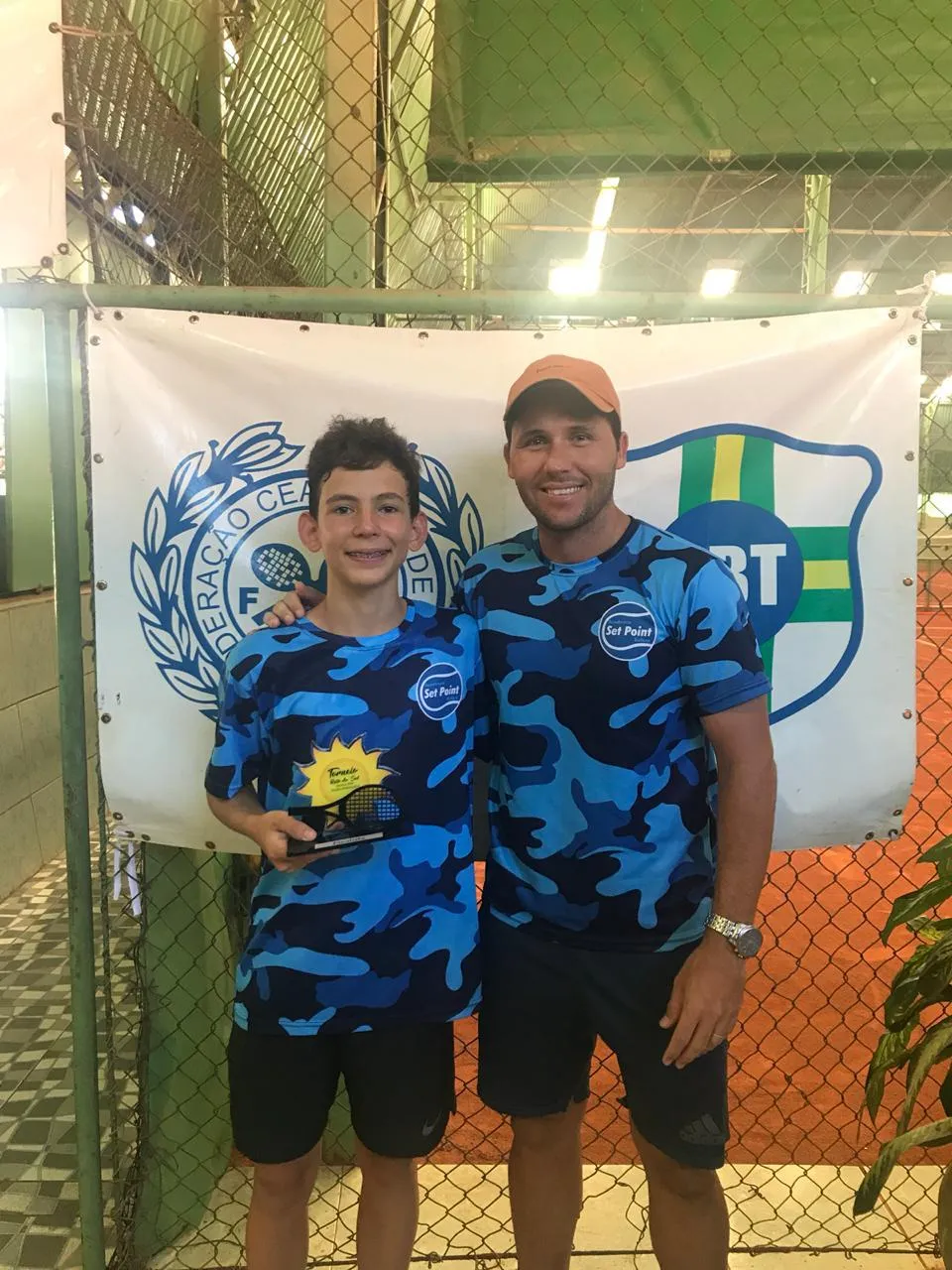 Arthur at 12, holding a trophy next to his coach in front of a tennis federation banner